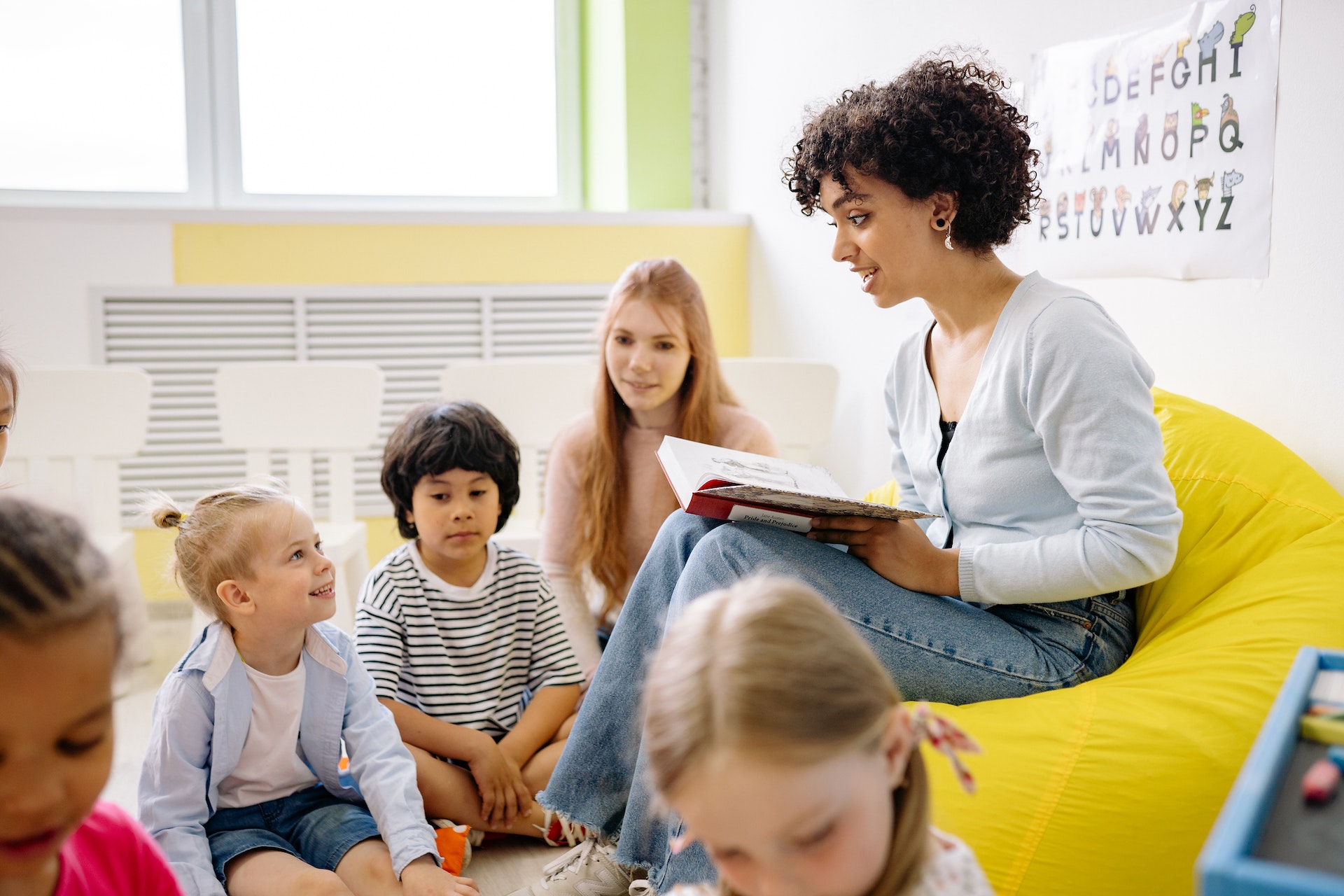 Une femme lit un livre à de jeunes enfants dans une activité d’éveil et de lecture pour la petite enfance.
